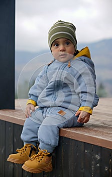 Portrait of an adorable baby boy wearing blue overall and yellow safety boots while sitting outdoors