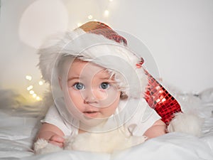 Adorable baby girl in Santa hat lying on the bed and smiling