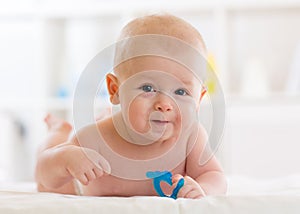 Portrait of adorable baby. Kid boy lying on his stomach and holding teether toy.