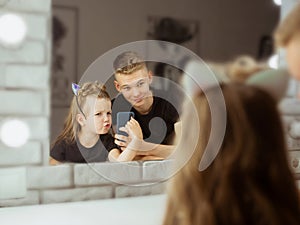 Portrait of adorable beautiful caucasian siblings brother and sister doing selfie in the make up mirror.