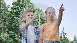 Portrait adorable boy and beautiful girl with long hair pointing away holding hands near the swing, smiling happily. A