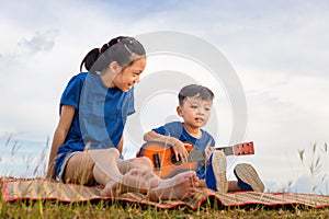 Portrait of adorable brother and sister playing outdoors. Asian kids singing songs in the garden, Happy boy and girl with guitar