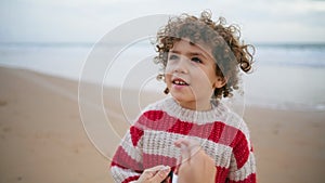 Portrait adorable curly boy resting beach with mother. Focused child hold kite