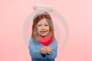 Portrait of adorable cute preschool girl with angelic nimbus holding paper heart and smiling to camera
