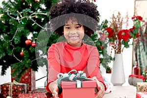 Portrait of adorable happy smiling African American girl child with black curry hair holding Christmas present gift box under
