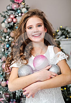 Portrait of adorable happy smiling little girl child in princess dress holding christmas balls near fir tree