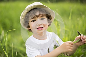 Portrait of adorable kid boy with hat standing on a summer meadow