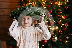 Portrait of adorable little blonde curly child girl holding Christmas standing in dark cozy room with festive interior.