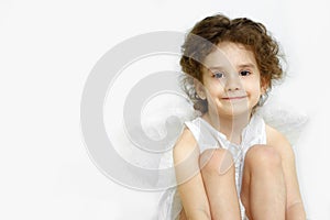 Portrait of adorable little girl with angelic face and smile in white dress and wings, isolated on white background.