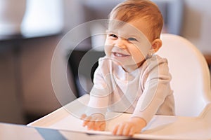 Portrait of adorable little girl on highchair. Baby laughing and play. Happy girl smile