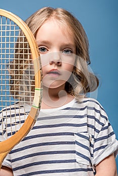 portrait of adorable little girl holding tennis raquet and looking at camera