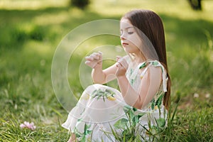 Portrait of adorable little girl sits barefoot on the grass in the park. Happy kid on the fresh air