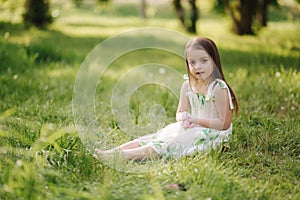 Portrait of adorable little girl sits barefoot on the grass in the park. Happy kid on the fresh air