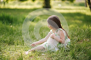 Portrait of adorable little girl sits barefoot on the grass in the park. Happy kid on the fresh air. End of quarantine