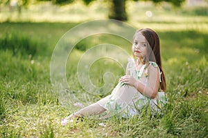 Portrait of adorable little girl sits barefoot on the grass in the park. Happy kid on the fresh air. End of quarantine
