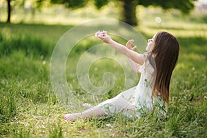 Portrait of adorable little girl sits barefoot on the grass in the park. Happy kid on the fresh air. End of quarantine