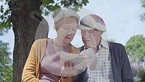Portrait adorable mature woman and man looking old photos remembering happy moments sitting on a bench in the park