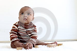 Portrait of adorable six month crawling African American baby playing with wooden developmental toys on fluffy white rug, happy