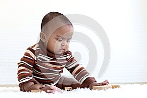 Portrait of adorable six month crawling African American baby playing with wooden developmental toys on fluffy white rug, happy