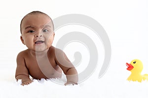 Portrait of adorable six month crawling African American baby playing with yellow duck toy on fluffy white rug, happy smiling