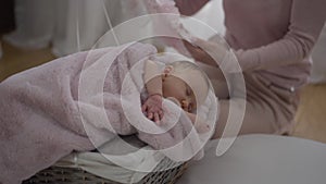 Portrait of adorable sleeping infant in baby basket with unrecognizable woman holding beautiful child dress at