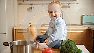 Portrait of adorable smiling baby boy sitting on kitchen table full of fruits and vegetables