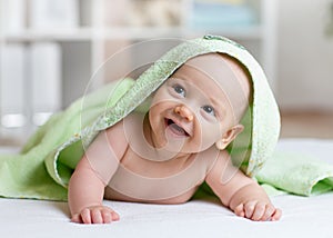 Portrait of adorable smiling baby in hooded towel lying on bed after having bathtime