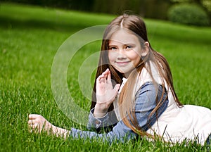 Portrait of adorable smiling little girl child preteen lying on grass in the park