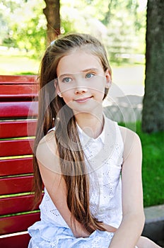 Portrait of adorable smiling little girl child schoolgirl teenager sitting on the bench outdoors