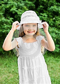 Portrait of adorable smiling little girl in white dress and hat