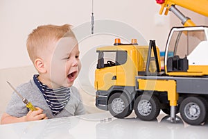 Portrait of adorable smiling toddler boy sitting at the table playing with a big construction car at home. Little child with toy