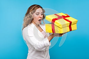 Portrait of adorable surprised woman peeking with curious amazed look into gift box. blue background