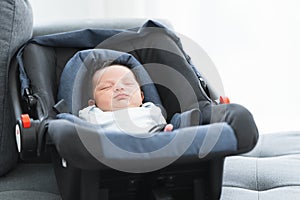 Portrait of adorable less than one month old newborn baby girl sleeping in the modern car seat with fastening safety belt at home