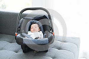 Portrait of adorable less than one month old newborn baby girl sleeping in the modern car seat with fastening safety belt at home