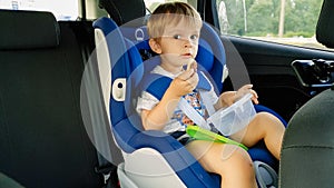 Portrait of adorable toddler boy sitting in child car safety seat and eating cookies