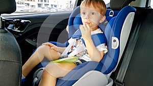 Portrait of adorable toddler boy sitting in child car safety seat and eating cookies