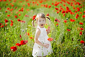 Portrait of an adorable toddler girl is surprised in a white dress play in a beautiful field of red poppies