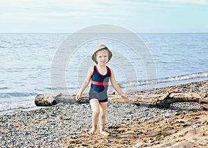 Portrait of adorable white Caucasian one toddler little girl with hat on her head going on lake sea gravel beach