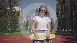 Portrait of adorable woman with a skateboard looking at the camera standing on the basketball court outdoors outdoors