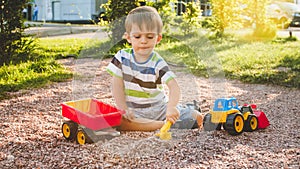 Portrait of adorable 3 years old toddler boy playing with toy truck with trailer on the playground at park. Child