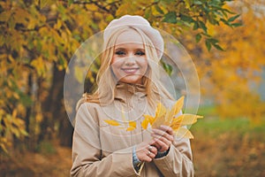 Portrait of adorable young happy blonde woman wearing french beret with autumn leaves outddor
