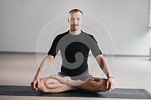 Portrait of an adult athletic man sitting in the lotus position in the gym on the mat