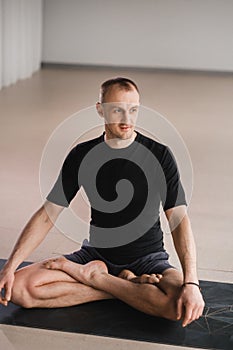 Portrait of an adult athletic man sitting in the lotus position in the gym on the mat