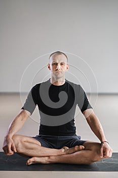 Portrait of an adult athletic man sitting in the lotus position in the gym on the mat