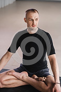 Portrait of an adult athletic man sitting in the lotus position in the gym on the mat