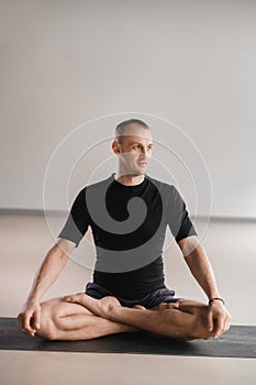 Portrait of an adult athletic man sitting in the lotus position in the gym on the mat