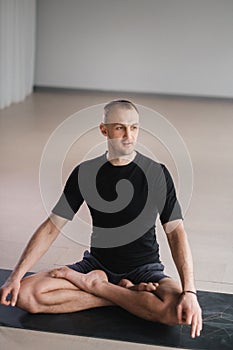 Portrait of an adult athletic man sitting in the lotus position in the gym on the mat