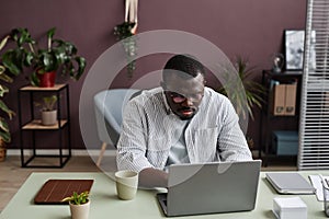 Adult black man using laptop in minimal office decorated with live green plants