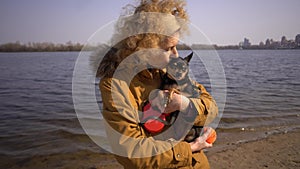 Portrait of an adult blonde curly hair Caucasian woman holding a small black-colored dog breed toy terrier. Old funny