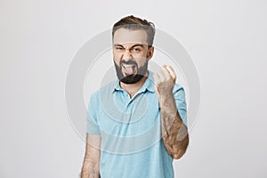 Portrait of adult bully, showing his fist and sticking out tongue with annoyed expression, over gray background. Come on